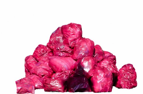 A pile of bright pink plastic rubbish bags, irregular in shape and tightly knotted at the top, stacked on top of each other in an outdoor setting. The bags are made of thin, shiny plastic material reflecting light, with some appearing slightly crumpled or stretched. They rest on a pavement or driveway surface with a neutral background, possibly in a residential or commercial area within Hoxton, London. The scene depicts waste ready for collection or disposal, aligning with rubbish removal services such as those offered by Hoxton House Clearance in the area. No other objects or elements are visible in the image, which focuses solely on the collection of refuse bags.