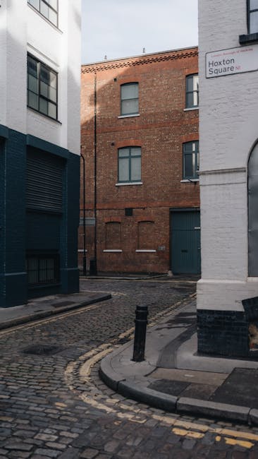 The image depicts the exterior of a white brick building with a large, arched window divided into multiple panes, some of which are obscured by reflections or objects inside. Below the window, there i